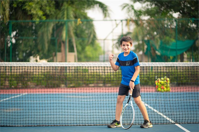 A boy, full of confidence, holds his tennis racket at the best school in Gurugram, ready for a fun game.